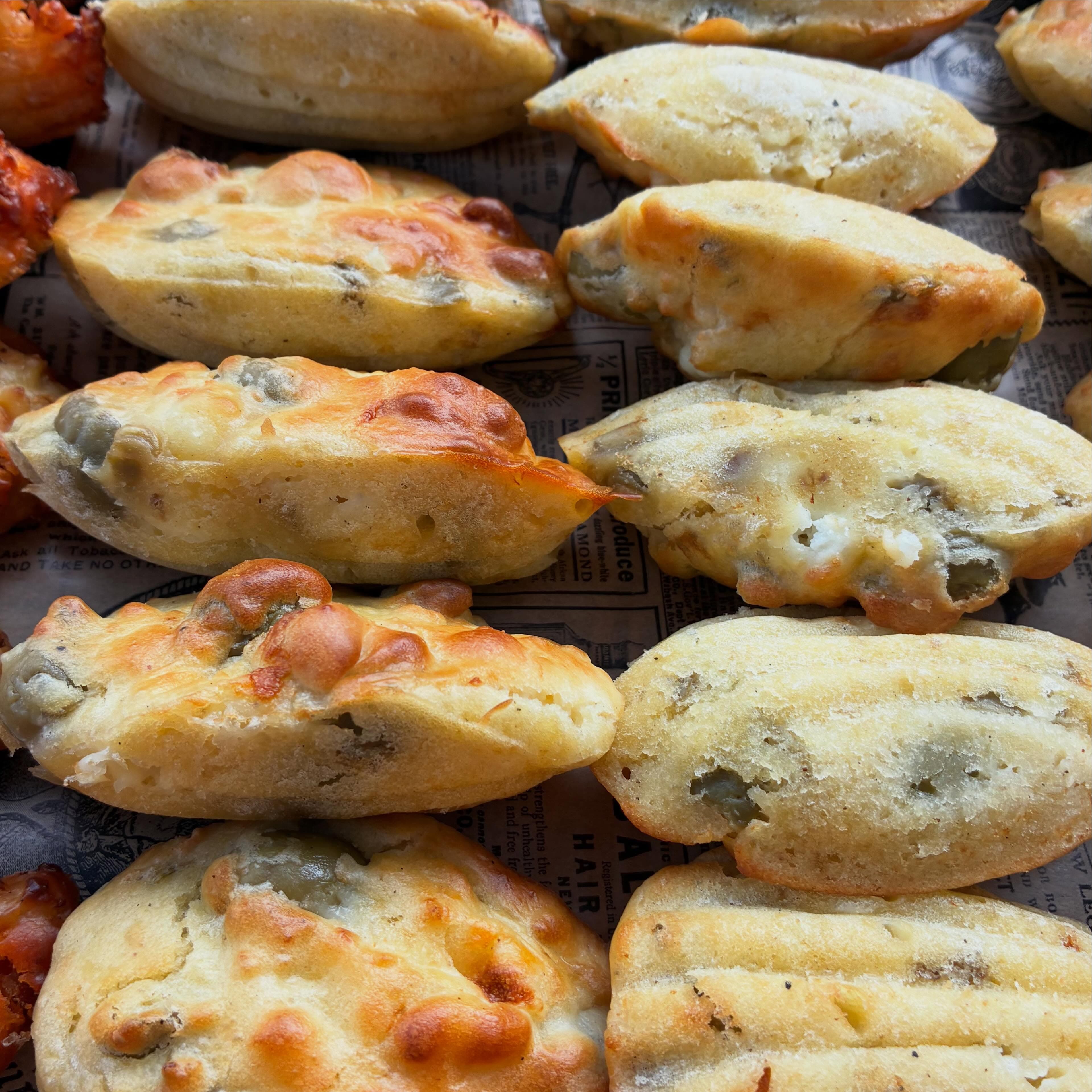 Madeleines salées olive et féta gratinées, rangées sur du papier journal imprimé