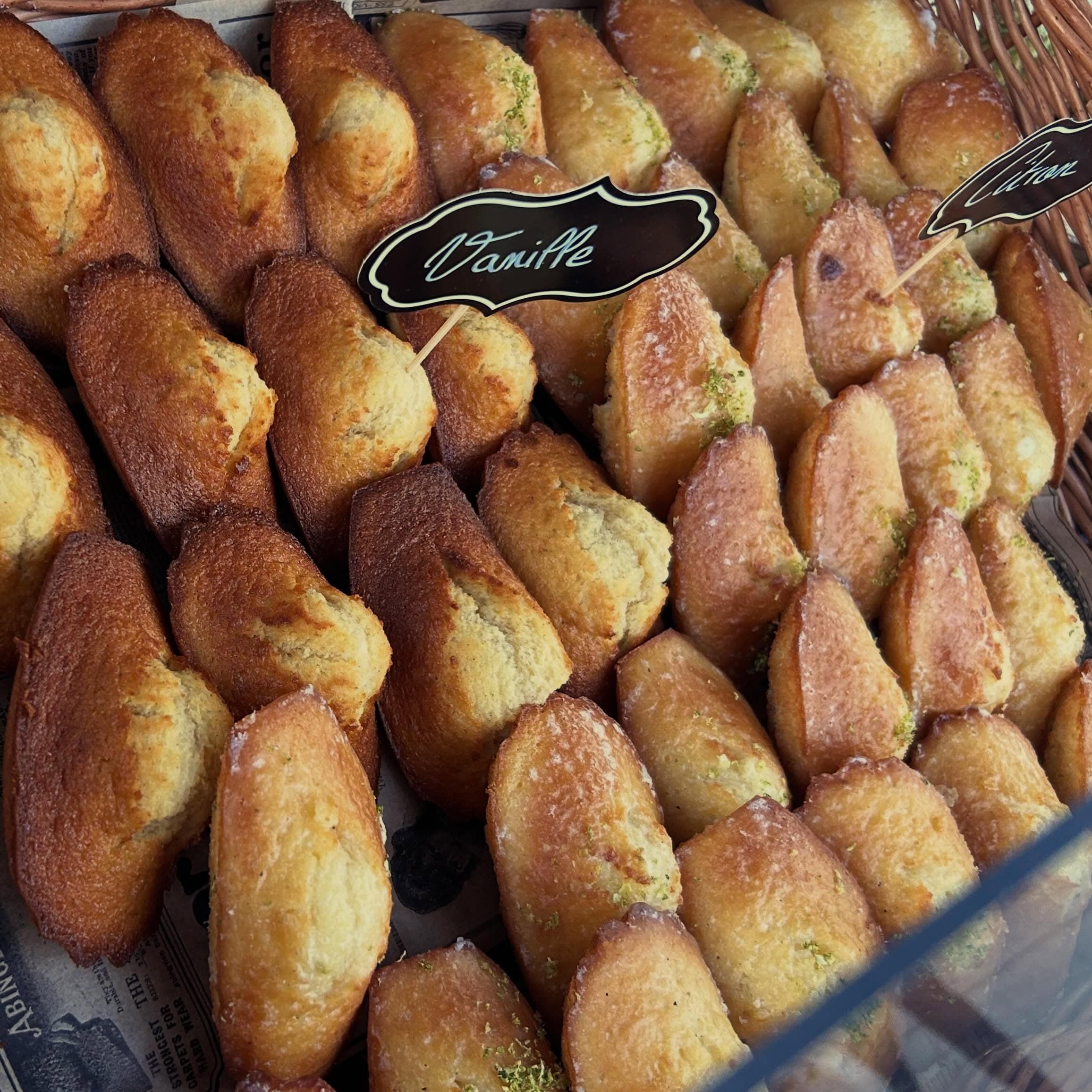 Madeleines vanille et citron dorées, zestes de citron vert, rangées dans un panier en osier avec leurs étiquettes écrites à la main